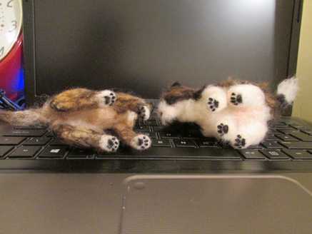 A needle felted brindle dog and Shih Tzu lying down with paws showing