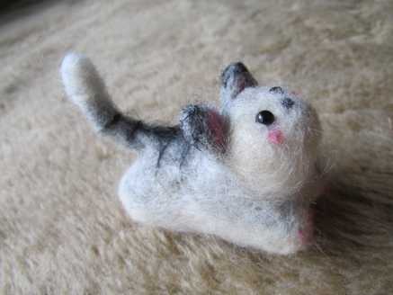 Side view of a needle felted grey cat with pink cheeks lying on carpet