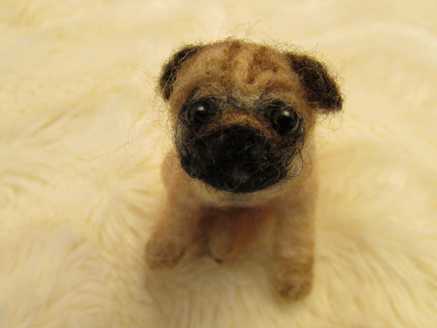 A needle felted brown pug sitting down