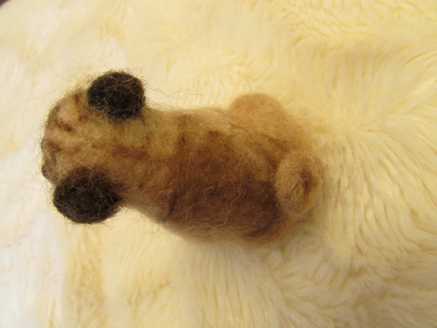 Behind view of a needle felted brown pug sitting down on carpet