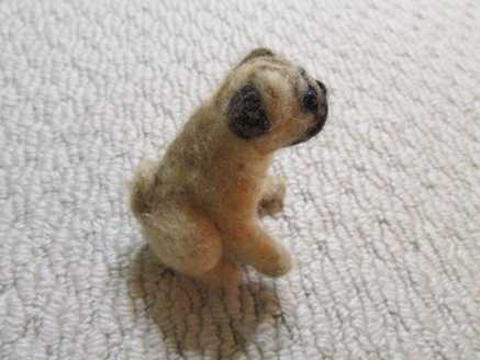 Side view of a needle felted brown pug sitting down on carpet