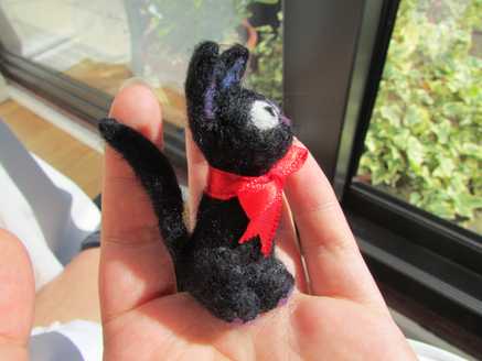 Side view of a needle felted black cat with a ribbon