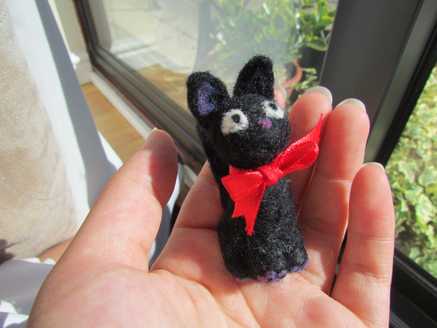 A needle felted black cat with a ribbon