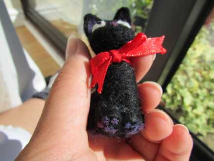 Underside view of a needle felted black cat with a ribbon
