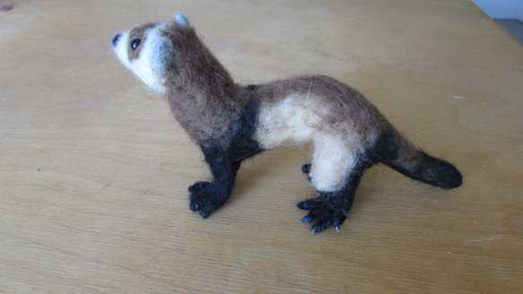 Sideview of a needle felted brown ferret standing on a table